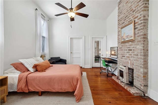 bedroom featuring wood finished floors, a fireplace, heating unit, and ceiling fan