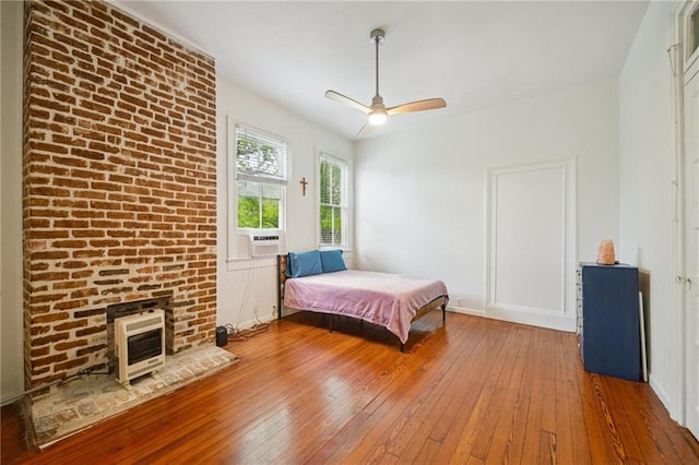 bedroom with hardwood / wood-style floors, heating unit, a fireplace, and a ceiling fan