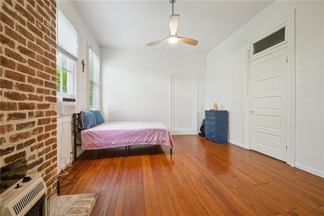 bedroom featuring wood-type flooring, heating unit, and a ceiling fan