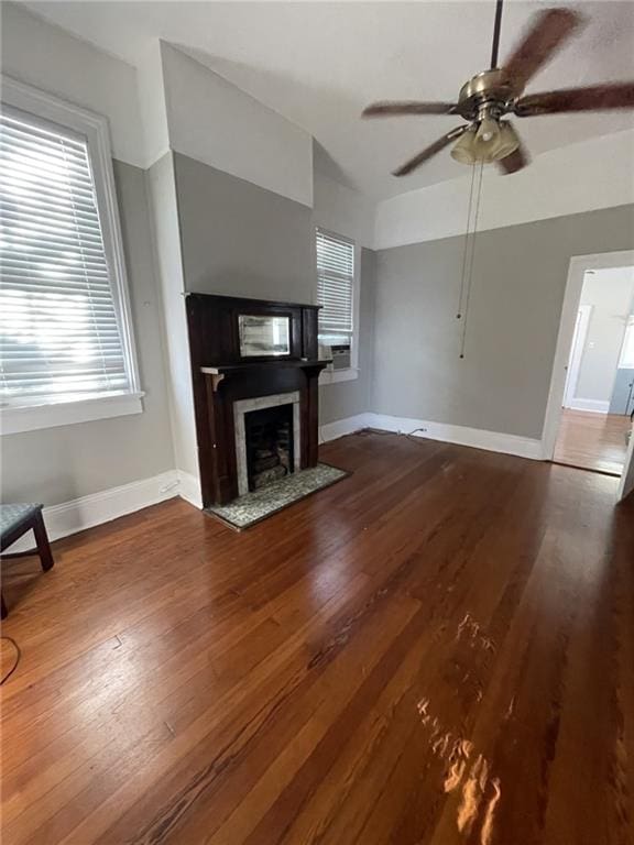 unfurnished living room with a ceiling fan, baseboards, wood finished floors, and a fireplace with flush hearth