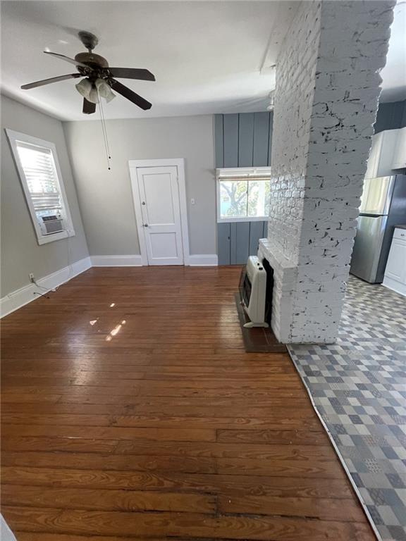 unfurnished living room featuring hardwood / wood-style flooring, heating unit, a ceiling fan, and plenty of natural light