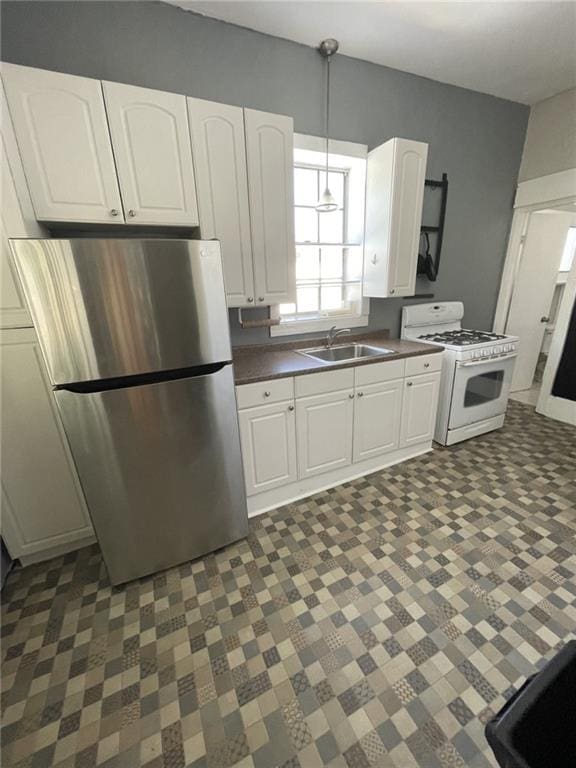 kitchen featuring white range with gas cooktop, freestanding refrigerator, a sink, and dark flooring
