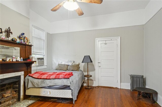 bedroom featuring wood finished floors, cooling unit, a fireplace, ceiling fan, and baseboards