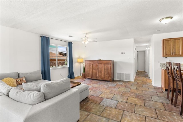 living area with baseboards, a textured ceiling, ceiling fan, and stone finish floors