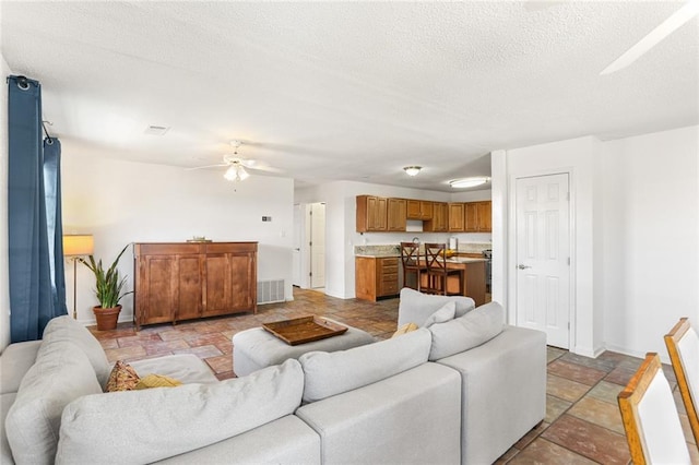 living room with a ceiling fan, light stone finish flooring, baseboards, and a textured ceiling