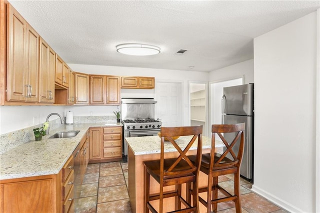 kitchen featuring stainless steel appliances, a sink, light stone countertops, a kitchen island, and a breakfast bar area