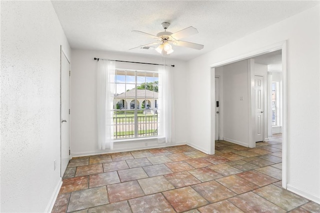 spare room featuring baseboards, ceiling fan, a textured ceiling, and stone finish flooring