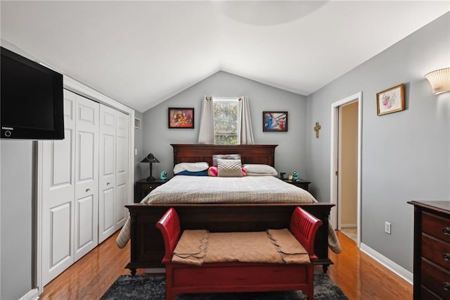 bedroom with light wood-style floors, lofted ceiling, a closet, and baseboards