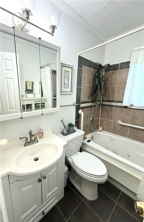 4560 Laine Ave, New Orleans, LA 70126 - bathroom featuring tile patterned flooring, a textured ceiling, toilet, a combined bath / shower with jetted tub, and vanity
