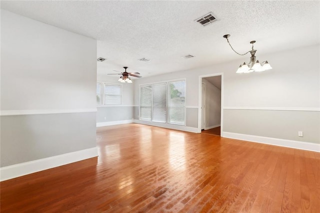 empty room featuring a chandelier, a textured ceiling, light wood finished floors, baseboards, and ceiling fan