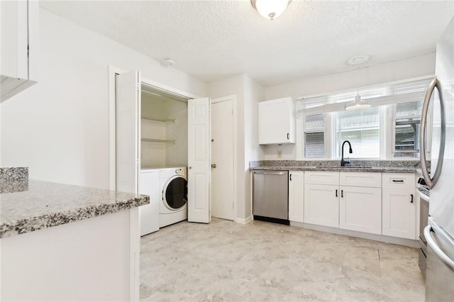 kitchen with stainless steel appliances, a sink, washer / dryer, white cabinetry, and a textured ceiling