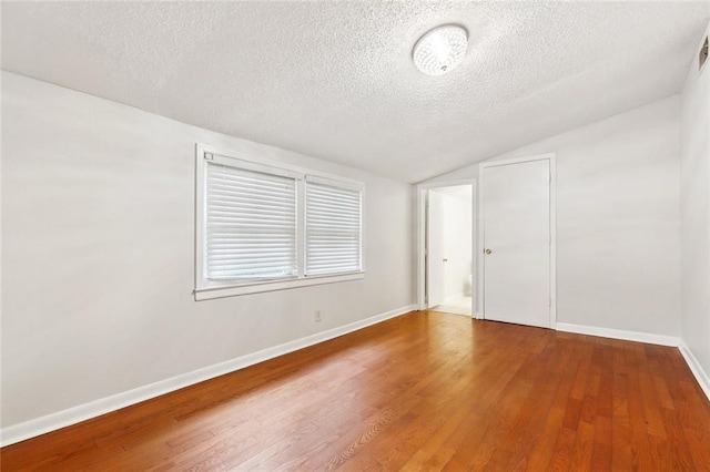 spare room featuring vaulted ceiling, a textured ceiling, wood finished floors, and baseboards