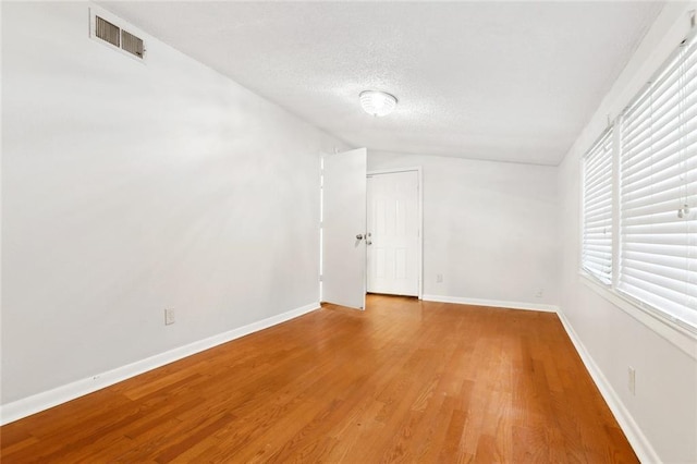 unfurnished room with lofted ceiling, light wood-type flooring, baseboards, and a textured ceiling