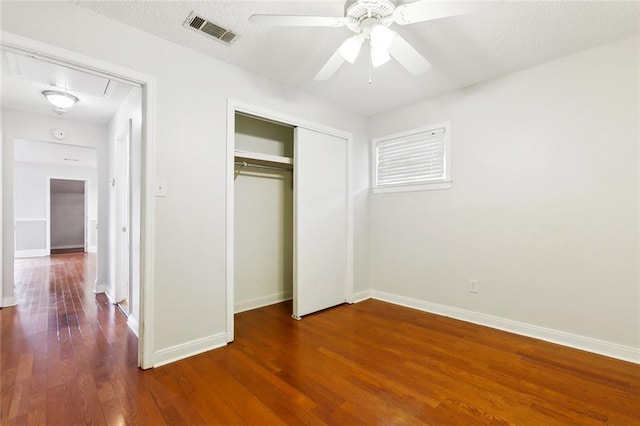 unfurnished bedroom featuring wood finished floors, baseboards, a closet, a ceiling fan, and attic access