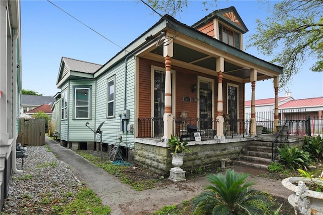 shotgun-style home with covered porch, metal roof, and fence