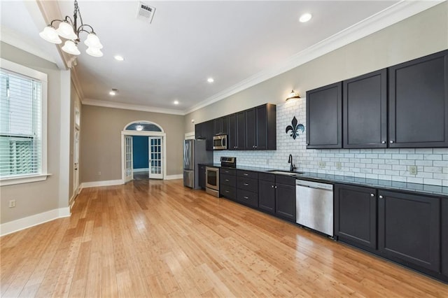 kitchen with appliances with stainless steel finishes, a sink, backsplash, light wood-style floors, and baseboards