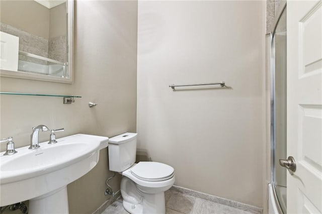 bathroom with toilet, tile patterned floors, a sink, bath / shower combo with glass door, and baseboards