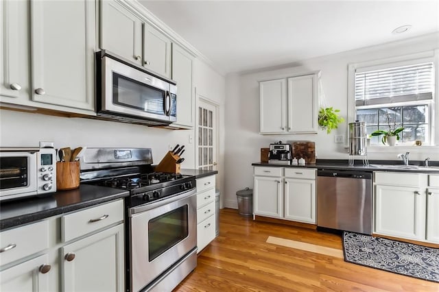 6817 Catina St, New Orleans, LA 70124 - kitchen featuring stainless steel appliances, a sink, light wood-style flooring, dark countertops, and white cabinets