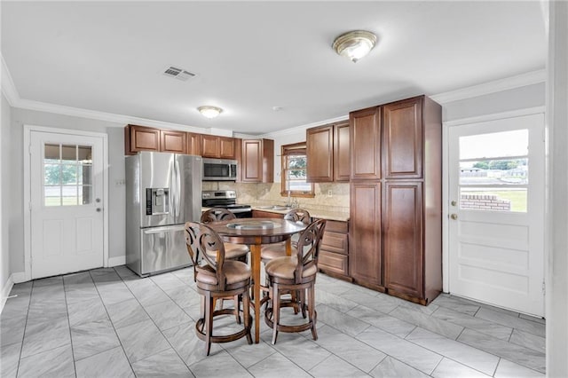 kitchen with stainless steel appliances, ornamental molding, backsplash, brown cabinetry, and baseboards