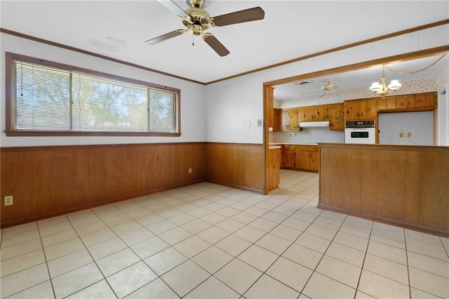 kitchen with white oven, brown cabinets, wainscoting, under cabinet range hood, and wood walls