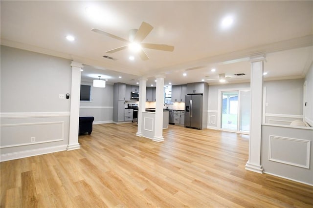unfurnished living room with ornate columns, ceiling fan, ornamental molding, light wood-type flooring, and a decorative wall