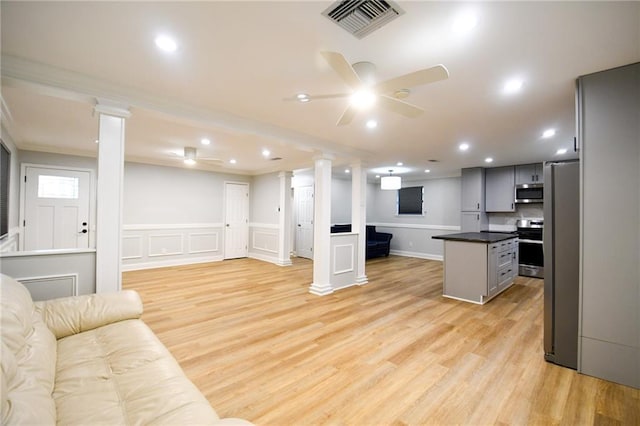 living room featuring ornate columns, a ceiling fan, light wood-style flooring, a decorative wall, and wainscoting