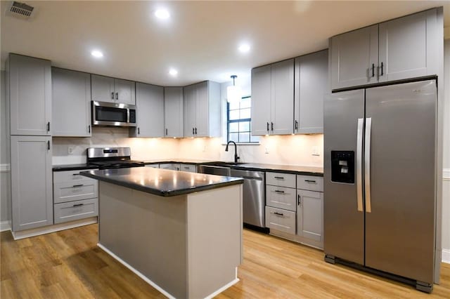 kitchen featuring appliances with stainless steel finishes, a sink, light wood-type flooring, dark countertops, and recessed lighting