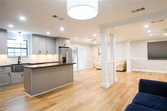 kitchen featuring open floor plan, stainless steel fridge with ice dispenser, a sink, gray cabinetry, and a decorative wall
