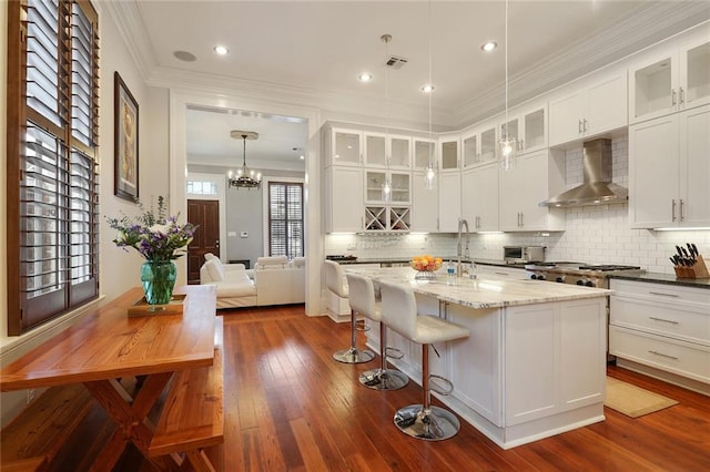 2026 Camp St, New Orleans, LA 70130 - kitchen with wall chimney range hood, crown molding, backsplash, an island with sink, and dark wood-style floors