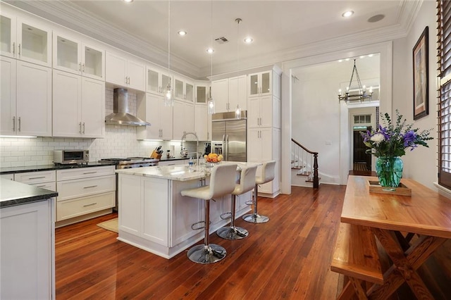 2026 Camp St, New Orleans, LA 70130 - kitchen featuring wall chimney exhaust hood, built in fridge, tasteful backsplash, ornamental molding, and white cabinetry
