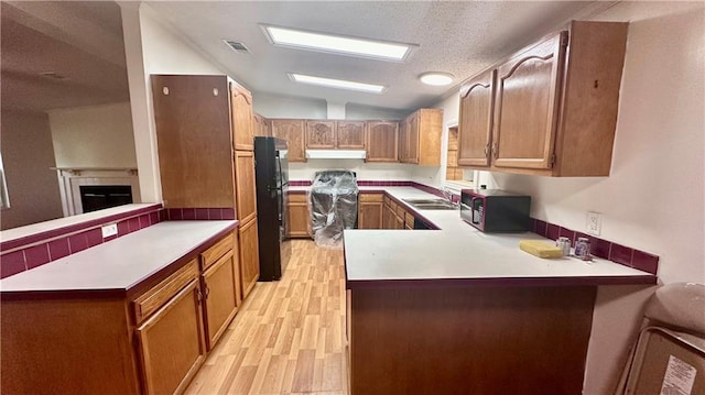 kitchen featuring black appliances, a peninsula, under cabinet range hood, light wood-style floors, and vaulted ceiling