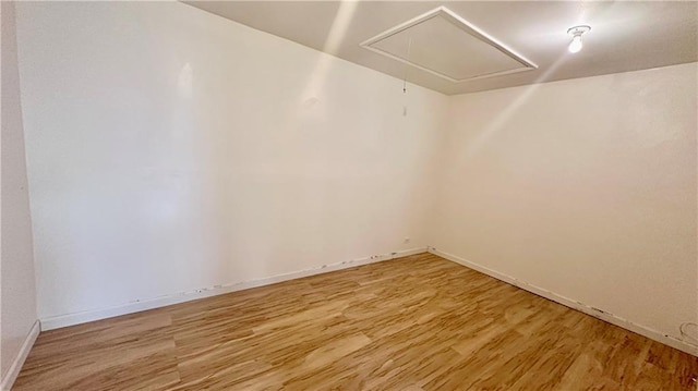 empty room featuring attic access, light wood finished floors, and baseboards