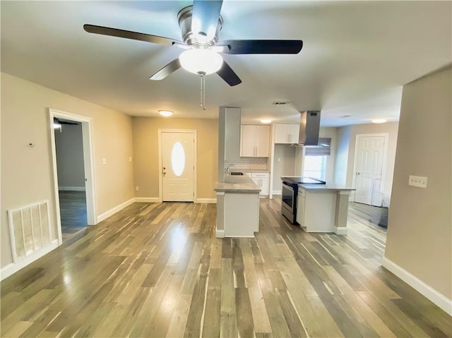 kitchen featuring stainless steel electric range oven, island range hood, white cabinets, ceiling fan, and wood finished floors
