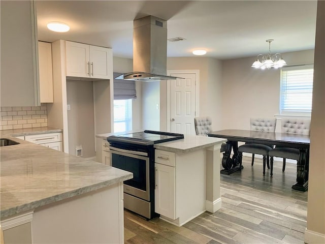kitchen with electric stove, island range hood, backsplash, light wood finished floors, and white cabinetry