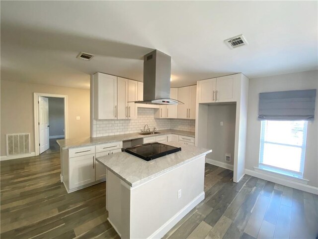 kitchen with island exhaust hood, a sink, white cabinets, and tasteful backsplash