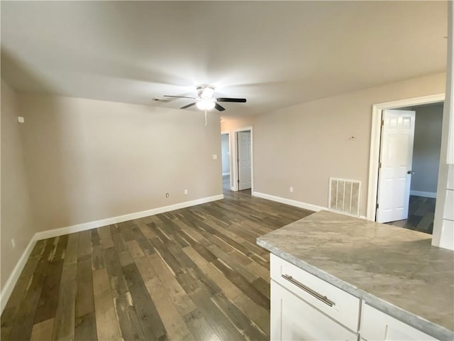 unfurnished room featuring dark wood-style flooring, a ceiling fan, and baseboards