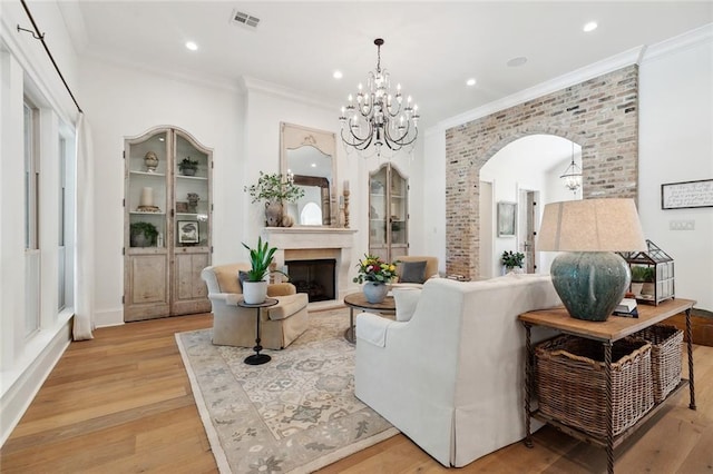474 Trailhead Dr, Abita Springs, LA 70420 - living area featuring arched walkways, light wood-style flooring, crown molding, a chandelier, and a fireplace with raised hearth