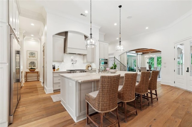 474 Trailhead Dr, Abita Springs, LA 70420 - kitchen featuring arched walkways, custom exhaust hood, ornamental molding, decorative backsplash, and an island with sink