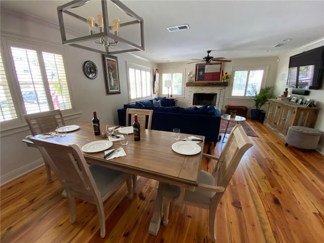 726 S Massachusetts St, Covington, LA 70433 - dining area with light wood-style flooring, a fireplace, a chandelier, ceiling fan, and ornamental molding
