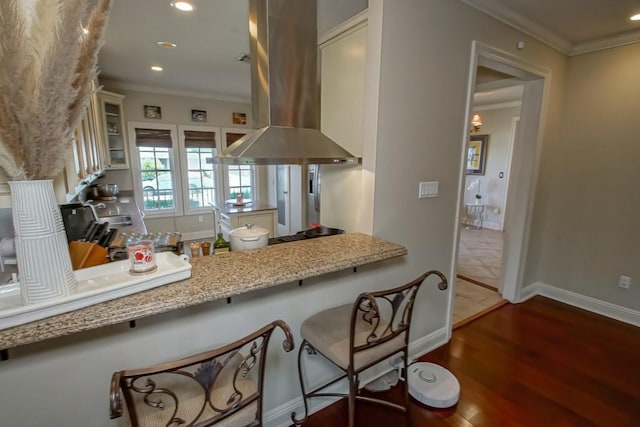 kitchen featuring island exhaust hood, ornamental molding, glass insert cabinets, recessed lighting, and wood finished floors