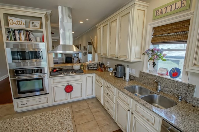 kitchen featuring stainless steel appliances, island range hood, a sink, cream cabinets, and light tile patterned flooring