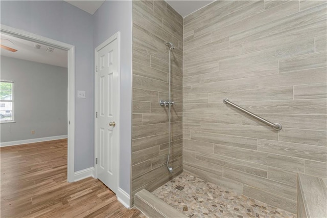 full bathroom with tiled shower, wood finished floors, and baseboards