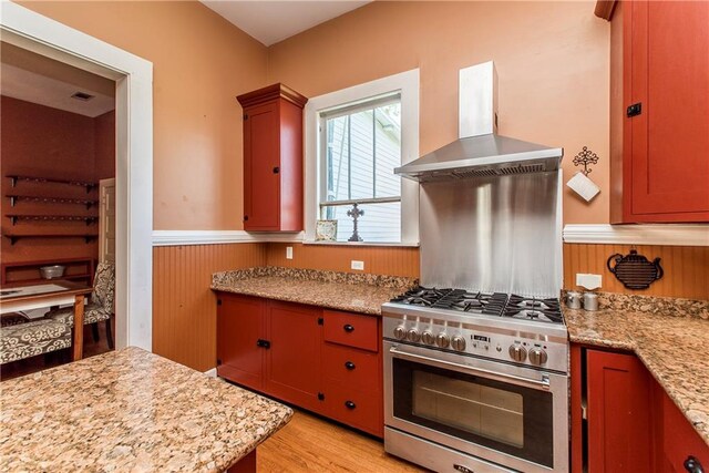 245 E Oak St, Ponchatoula, LA 70454 - kitchen with high end range, wall chimney exhaust hood, a wainscoted wall, light wood-type flooring, and light stone counters