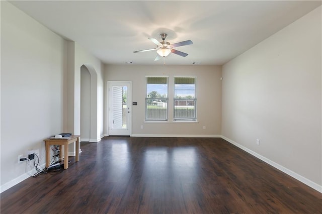 unfurnished living room featuring arched walkways, a ceiling fan, baseboards, and dark wood finished floors