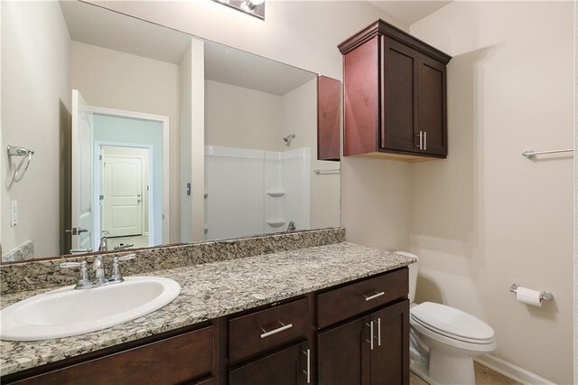 bathroom with a shower, toilet, vanity, and baseboards