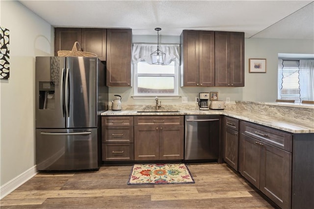 kitchen with stainless steel appliances, a sink, a peninsula, and light wood finished floors