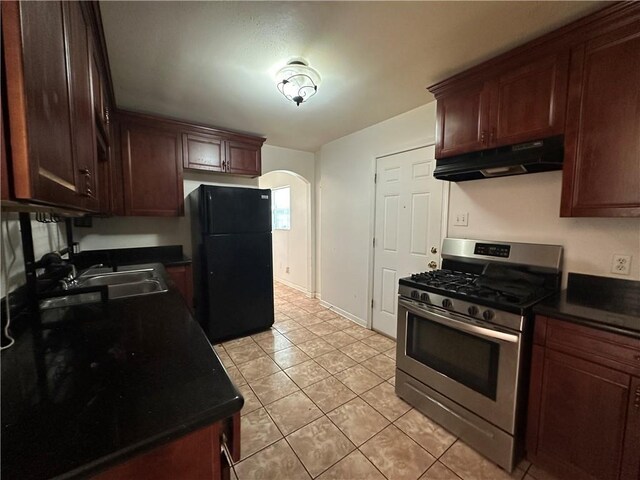 3855 Metropolitan St, New Orleans, LA 70126 - kitchen with freestanding refrigerator, under cabinet range hood, stainless steel range with gas stovetop, arched walkways, and dark countertops