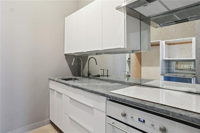 538 Governor Nicholls St, New Orleans, LA 70116 - kitchen with wall oven, white cabinetry, dark stone countertops, exhaust hood, and baseboards