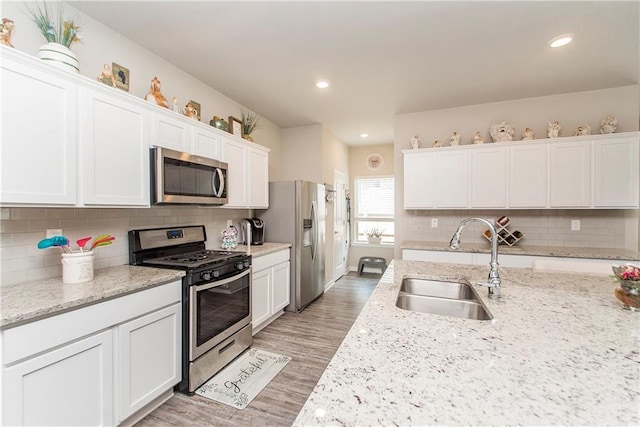 3663 Trestle Crossing Ave, Slidell, LA 70461 - kitchen with stainless steel appliances, a sink, white cabinets, light wood-style flooring, and decorative backsplash
