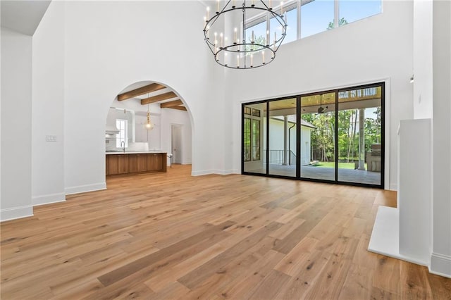 136 Linnette Ln, Mandeville, LA 70471 - unfurnished living room featuring a towering ceiling, a chandelier, arched walkways, light wood-type flooring, and baseboards